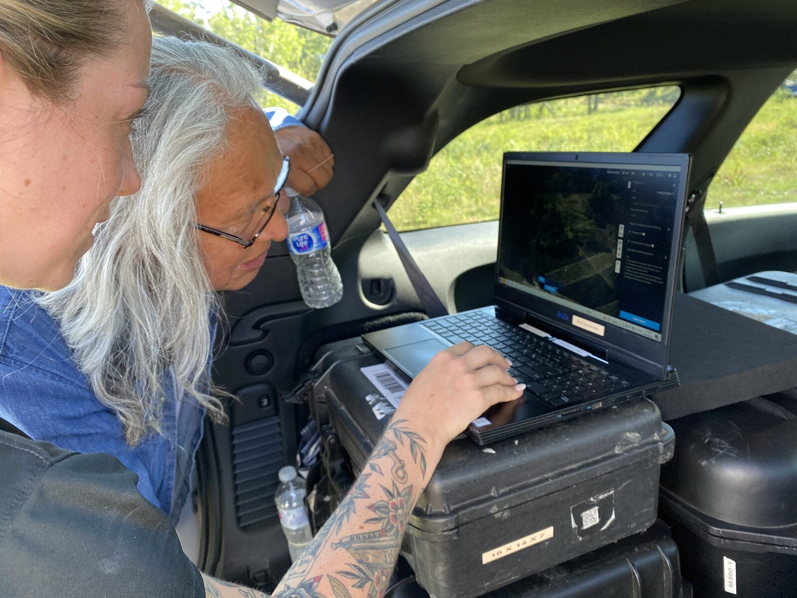Geospatial specialist reviewing drone imagery and spatial data on a laptop during fieldwork