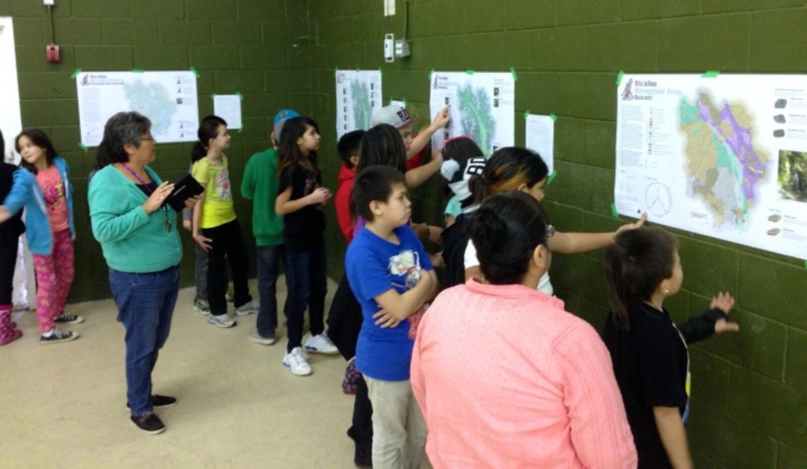 Community members of all ages reviewing printed atlas maps on a wall