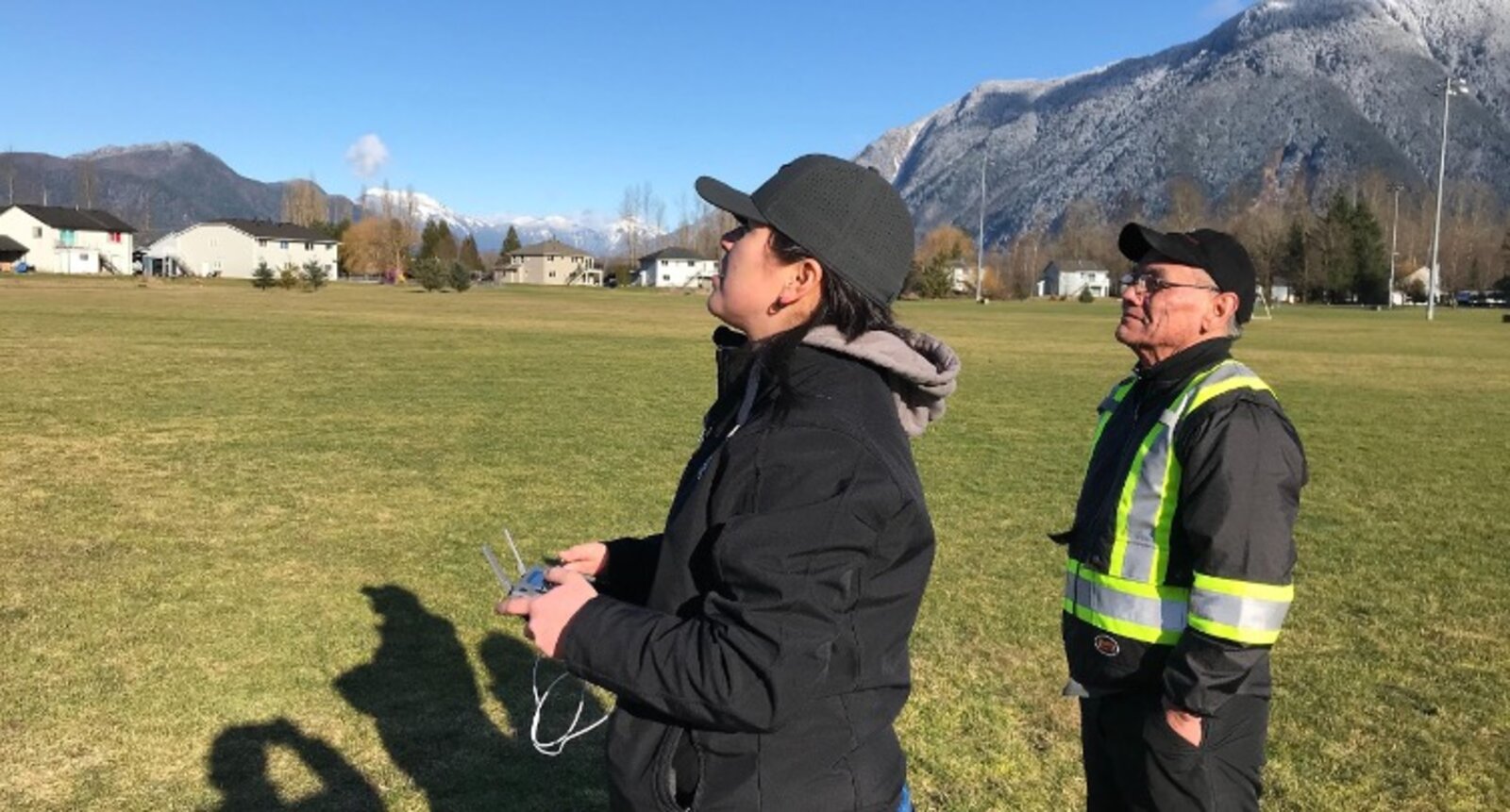 Trainee and instructor flying a drone in an open field with mountains behind